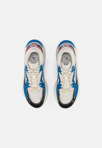 Baskets avec tige en mesh, accents bleus et rouges, semelle noire et base crème. Comporte des superpositions texturées et des détails réfléchissants.