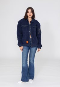 Granatowa polarowa kurtka z zapięciem na guziki, dwoma kieszeniami na piersi i kieszenią na suwak na ramieniu. Uzupełniona rozszerzonymi dżinsami i białymi butami.