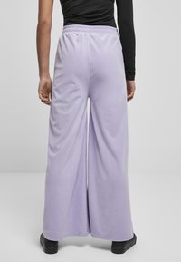 Lichtpaarse broek met wijde pijpen en een elastische tailleband, met een zachte textuur. De stof valt soepel en heeft minimale details.
