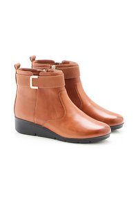 Bottines en cuir marron avec bord élastique, bande texturée et détails en métal doré. Bout rond et petit talon noir. Fini lisse.