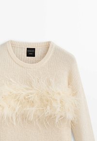 Pull en tricot de couleur crème avec un col rond et une rangée horizontale de garniture en plumes duveteuses traversant la poitrine.