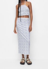 Ensemble deux pièces fleuri comprenant un haut court ajusté à col halter et une longue jupe, tous deux blancs avec des motifs floraux bleus.