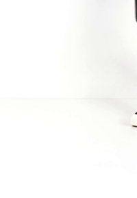 Osoba u crnim hlačama i crno-bijelim tenisicama stoji na bijeloj pozadini, vidljivi su samo donji dijelovi nogu i stopala.