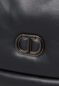 Svart lærveske med et gullfarget dobbelt D-logo og strukturert overflate. Solid lås og minimalistisk design uten ekstra metalldetaljer.