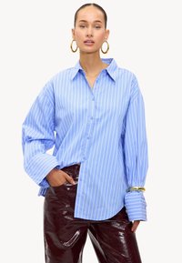 Blauw gestreefd overhemd met oversized mouwen, gecombineerd met glanzende bordeauxrode broek. Bevat een klassieke kraag en een loose fit.