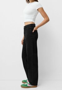 Vaqueros anchos negros con cintura alta, combinados con una camiseta ajustada blanca y zapatillas verdes con detalles en rosa.