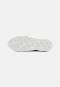 Sneaker bianco con suola in gomma testurizzata che presenta un motivo zigzag. Il design è semplice e raffinato, adatto per il tempo libero.