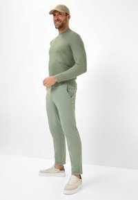 Hellgrüner, taillierter Pullover mit weicher Textur; kombiniert mit passenden, schmal geschnittenen Hosen. Cremefarbene Sneaker mit braunen Akzenten runden das Outfit ab.