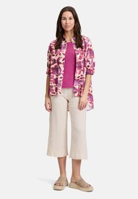 Koszulka z krótkim rękawem w różowy kwiatowy wzór, lekka, nałożona na jednolity różowy sweter. Lnianie, beżowe spodnie o szerokich nogawkach, długości 7/8 oraz sandały.