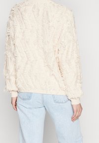 Kermakollane sviiter, millel on tekstureeritud ja kulunud muster; ribidega mansetid ja paar; lahti lõige; kantud helesiniste teksadega.