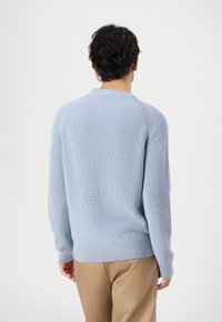 Light blue knitted sweater with a ribbed texture, featuring a round neckline and raglan sleeves. The hem is slightly stretchy.