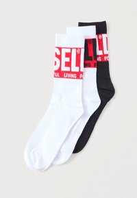 Bomullsblandede sokker i hvitt, svart og grått, med kontrasterende røde logoer. Ribbet tekstur med midt-på-leggen design.