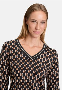 Top a V scollo con maniche lunghe, caratterizzato da un motivo geometrico in beige e marrone su fondo nero; tessuto liscio con un collo a contrasto.