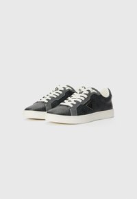 Black sneakers with textured fabric, white laces, and rubber sole. Features a triangular logo on the side and contrast stitching.