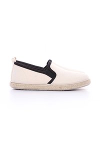 Baskets slip-on en toile avec une tige beige, des accents noirs et une semelle en jute tissée et texturée. Design minimaliste avec une languette au niveau du talon.
