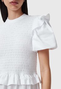 Witte top met een geplooide structuur bij het lijfje, korte ruches mouwen en een zoom met een franje detail. Vrouwelijk katoen materiaal.