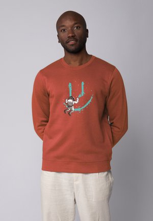 Ein sweatshirt in rostfarbenem, weichem Baumwollmaterial, das ein Cartoon-Astronautenmotiv mit türkisfarbenen Akzenten zeigt, mit rundem Halsausschnitt und gerippten Bündchen.