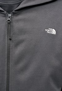 Γκρι φούτερ με φερμουάρ από λείο ύφασμα, με ψηλό γιακά, κεντημένο λογότυπο στο στήθος και λεπτ ομέρειες με μαύρο φερμουάρ.