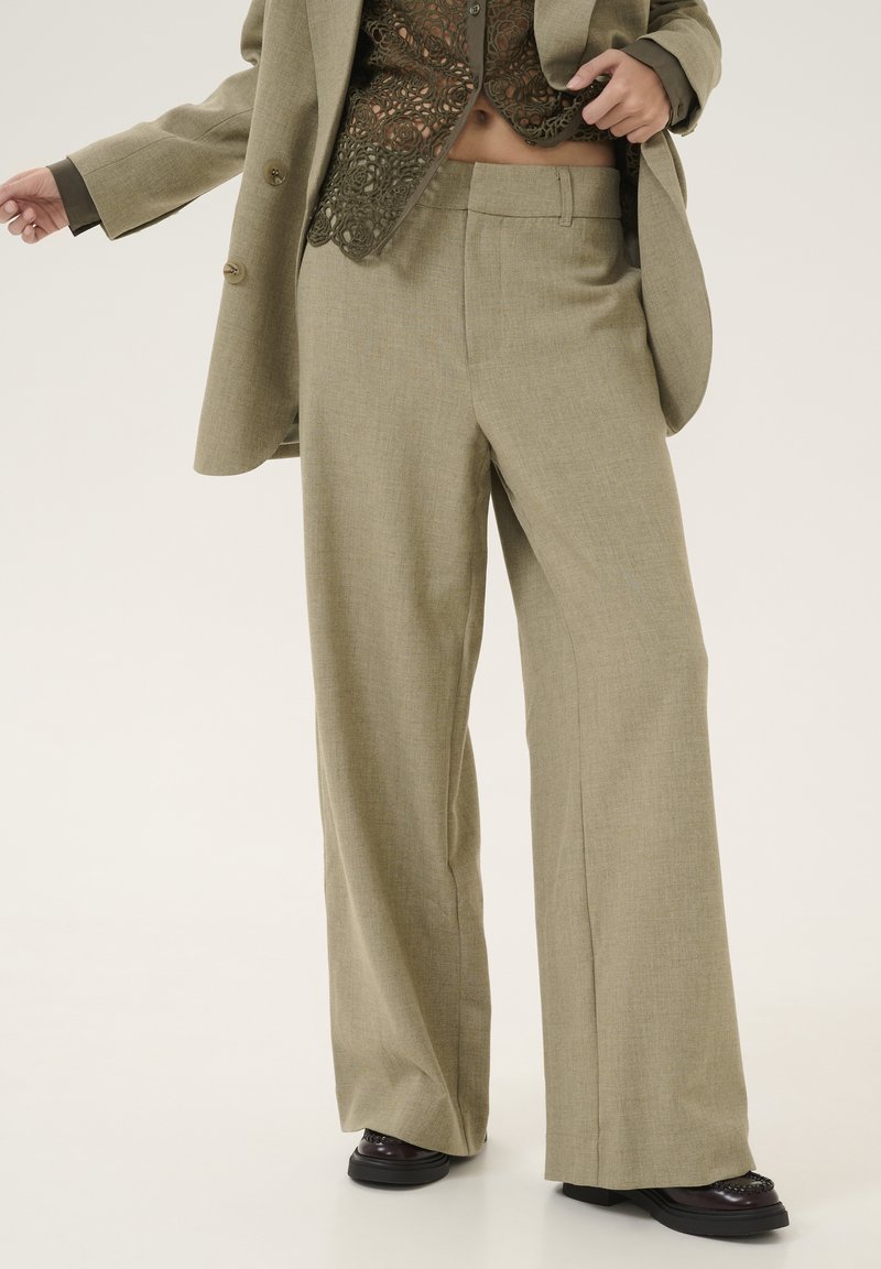 Pantalones de pierna ancha en un tejido de color verde oliva claro, con una textura sutil y líneas limpias. Combinados con una blusa de encaje más oscura.