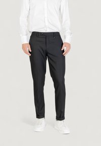 Pantalones negros ajustados con un corte slim, hechos de una tela suave, que cuentan con una cinturilla, bolsillos frontales y un diseño limpio. Combinados con zapatillas blancas.
