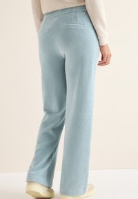 Jasnoniebieskie spodnie sztruksowe z wysokim stanem, szerokimi nogawkami i dwiema tylnymi kieszeniami, połączone z jasnymi sneakersami.