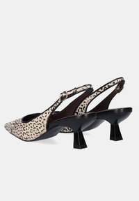Un par de zapatos de tacón con punta afilada y tiras de leopardo en color beige, con tacos de bloque negros y cierres de hebilla en tono dorado.
