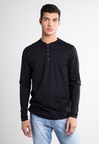 Fekete, hosszú ujjú henley póló, puha pamutból készült, kerek nyakkivágással, háromgombos gombolással és karcsú fazonnal.