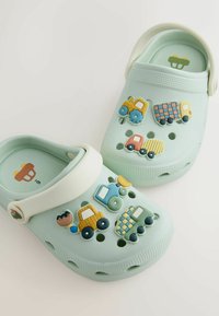 Svetlo mätové zelené dreváky s farebnými ozdobami v tvare vozidiel. Vyrobené z gumy, s ventilačnými otvormi a bielym remienkom.