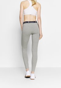 Szare legginsy z miękkiego materiału, z wysokim pasem i czarnym logo "Champion". W zestawie z białymi butami sportowymi.