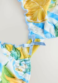 Bikini-top met een bloemontwerp in gele en blauwe kleuren, gerafelde randen en een lichtblauwe strikaccent op de band.