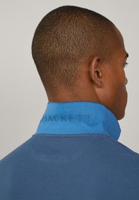 Modrá bavlněná polokošile s texturovaným límcem, na zadní straně s názvem značky "HACKETT" v tmavším odstínu. Hladká látka s příjemně přiléhavým střihem.