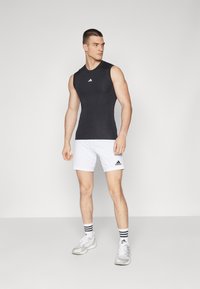 Black sleeveless athletic top with a fitted design, paired with white shorts featuring a black logo. Gray sneakers and striped socks complete the outfit.