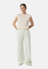 Hellrosa Bluse mit gefaltetem Kragen und kurzen, schwingenden Ärmeln, kombiniert mit weißen weiten Hosen. Glatter Stoff, taillierter Schnitt.