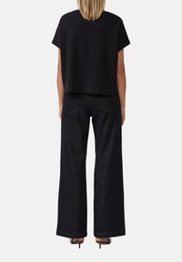 Zwarte cropped top met korte mouwen, gecombineerd met wijde, donkere denim jeans. De outfit heeft een minimalistisch ontwerp met strakke lijnen.