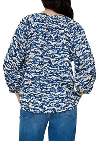 Blouse in blauw en crèmekleur met patroon, lange mouwen, gerimpelde halslijn, textuurstof en een ontspannen pasvorm, gecombineerd met blauwe denim jeans.