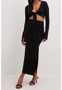 Conjunto de dos piezas en negro acanalado que incluye un top corto de manga larga con un lazo frontal y una falda maxi con una abertura alta; diseño ajustado.