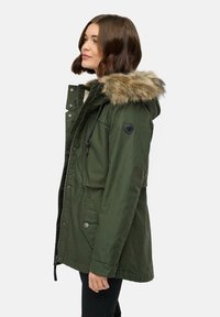 Olivgrön parka med fuskpäls på huvan, dragkedja och tryckknappar, sidofickor och justerbar midja. Mjuk textur och isolerad design.