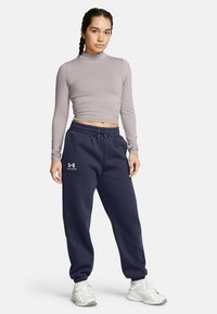 Enganliegendes, langärmeliges, hellgraues Oberteil kombiniert mit marineblauen Jogginghosen mit elastischem Bund und Logodetail. Weiße Sneakers runden das Outfit ab.