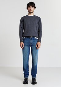 Maglietta grigia a maniche lunghe con colletto bianco, abbinata a jeans blu sbiaditi e stivaletti neri alla caviglia. Design a gamba dritta e linee pulite.