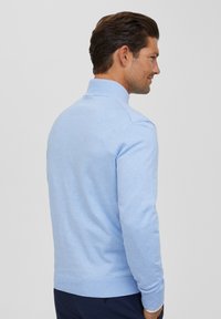 Jasnoniebieski sweter typu pulower, wykonany z miękkiej dzianiny, z wysokim kołnierzem, długimi rękawami oraz ściągaczami na mankietach i dolnym brzegu.