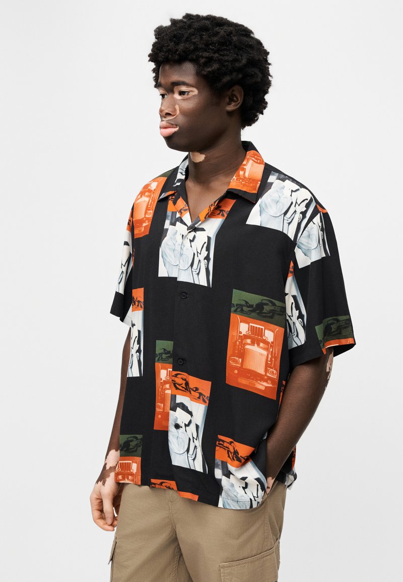 Camicia a maniche corte con bottoni, base nera con motivi grafici audaci in arancione, verde e bianco; vestibilità rilassata con tasche applicate.