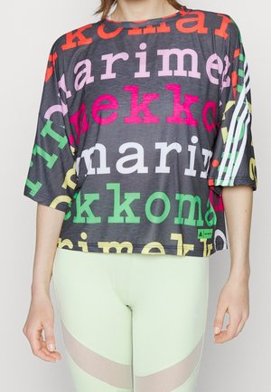Person trägt ein lockeres schwarzes Top mit buntem großem Schriftzug und weißen Streifen auf den Ärmeln, kombiniert mit hellgrünen Leggings mit Netzeinsätzen.