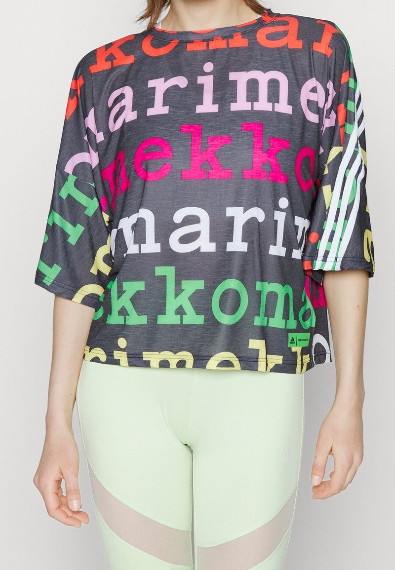 Personne portant un haut noir ample avec un grand texte coloré et des rayures blanches aux manches, associé à des leggings vert clair avec des panneaux en mesh.