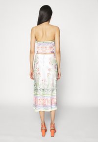 Robe midi à motif floral avec fines bretelles, dotée d'une fermeture éclair au dos, d'un corsage ajusté et d'une jupe fluide dans des tons blancs, verts et roses.