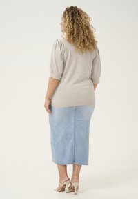 Lichtgrijze kortegangen trui met subtiele glans, gecombineerd met een middelmatig blauwe denimrok; model draagt beige hoge hakken.