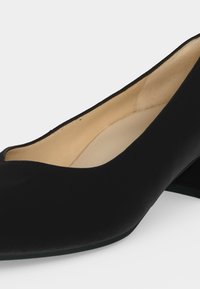 Chaussure femme noire à petit talon avec bout rond et doublure intérieure beige sur fond blanc.