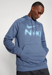 Modrá mikina Nike s textúrovanou tkaninou, klokanie vrecko, kapucňa so šnúrkou a svetlomodrý potlač loga na prednej strane.