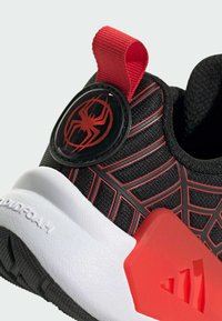 Crne tenisice s crvenim dizajnom paukove mreže, crvenim akcentima i crnim logom pauka na okrugloj oznaci. Imaju bijelu srednju potplat i teksturiranu vanjsku potplat.