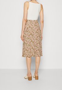 Jupe midi florale avec un fond marron, des motifs roses et verts, un ourlet évasé et une taille qui se ferme à l'arrière.