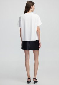 Camiseta blanca de manga corta con un corte relajado, que presenta un escote redondo. Combinada con una falda corta de imitación cuero negra y tacones negros.